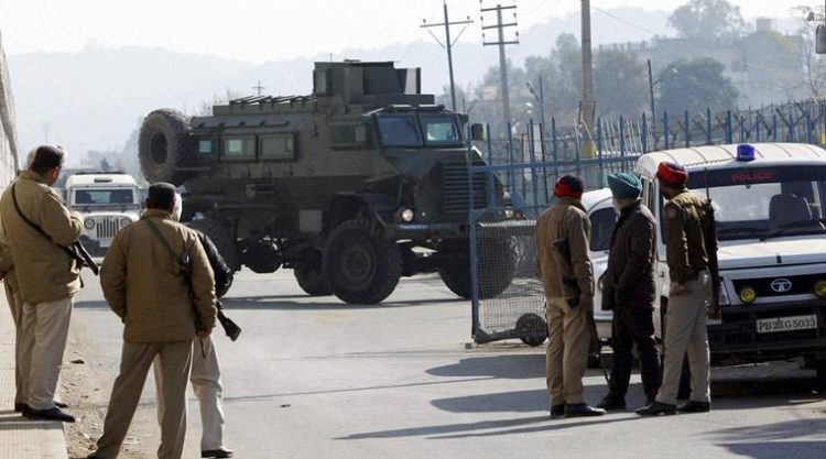 Pathankot:  Security men stand guard as an armored vehicle moves near the Indian Air Force base that was attacked by militants in Pathankot, Punjab on Saturday. PTI Photo  (PTI1_2_2016_000064B)