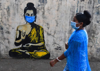 TOPSHOT - A resident wearing a facemask amid concerns over the spread of the COVID-19 novel coronavirus walks past a graffiti of Buddha wearing facemask, in Mumbai on March 16, 2020. (Photo by INDRANIL MUKHERJEE / AFP) (Photo by INDRANIL MUKHERJEE/AFP via Getty Images)